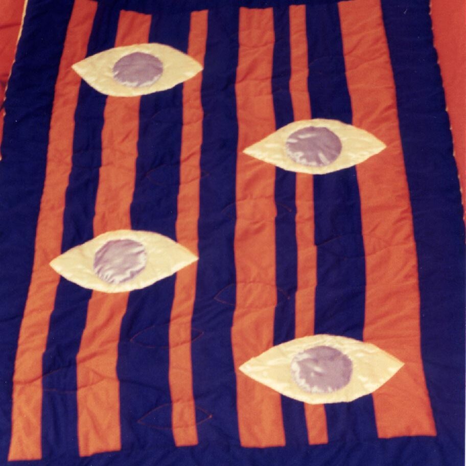 quilt with irregular navy and orange vertical stripes, and 4 overlaid eyes